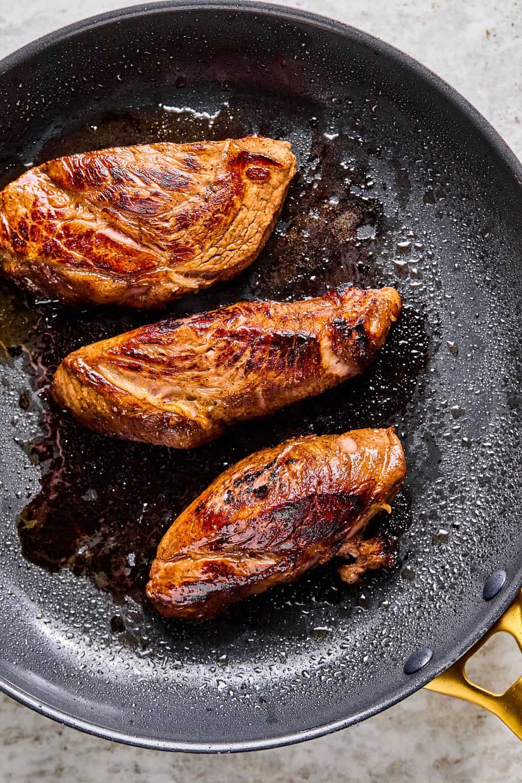 Three pieces of seared steak cook in a nonstick skillet, their browned, caramelized surfaces glistening with oil and cooking juices—perfect for adding rich flavor to your next steak pasta dish.