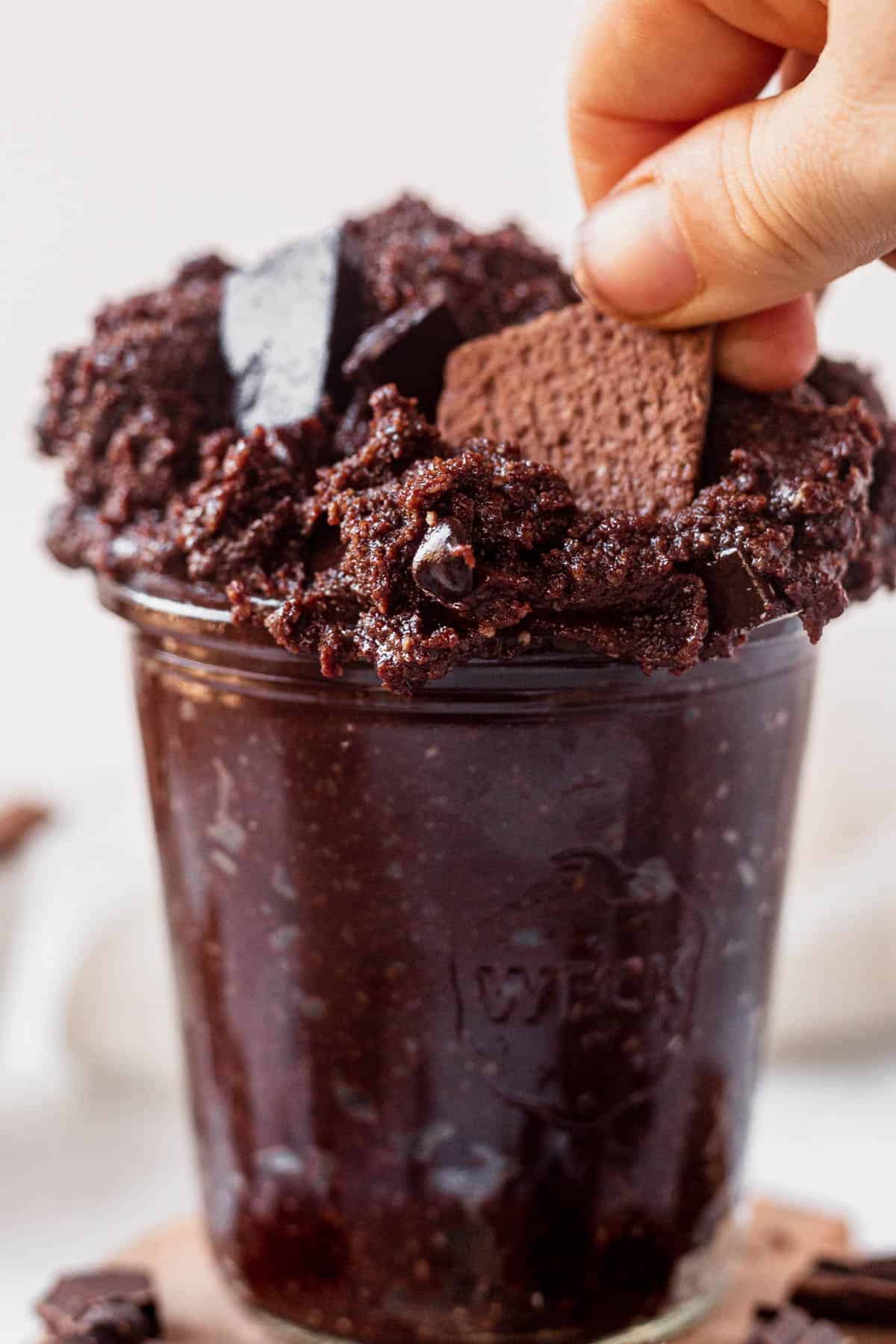 scooping edible brownie batter out of a jar with a chocolate cookie