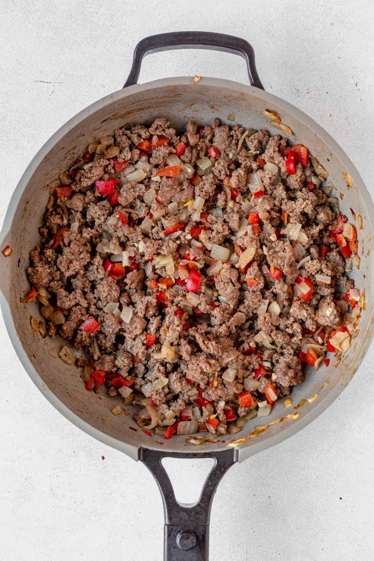 browned ground beef with peppers and onions in a skillet