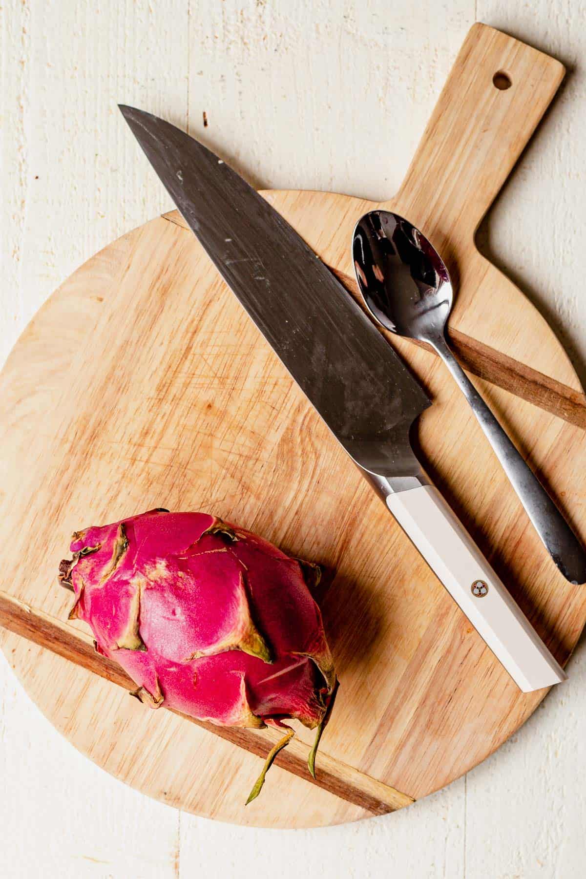 cutting board, knife, spoon and dragon fruit on a countertop