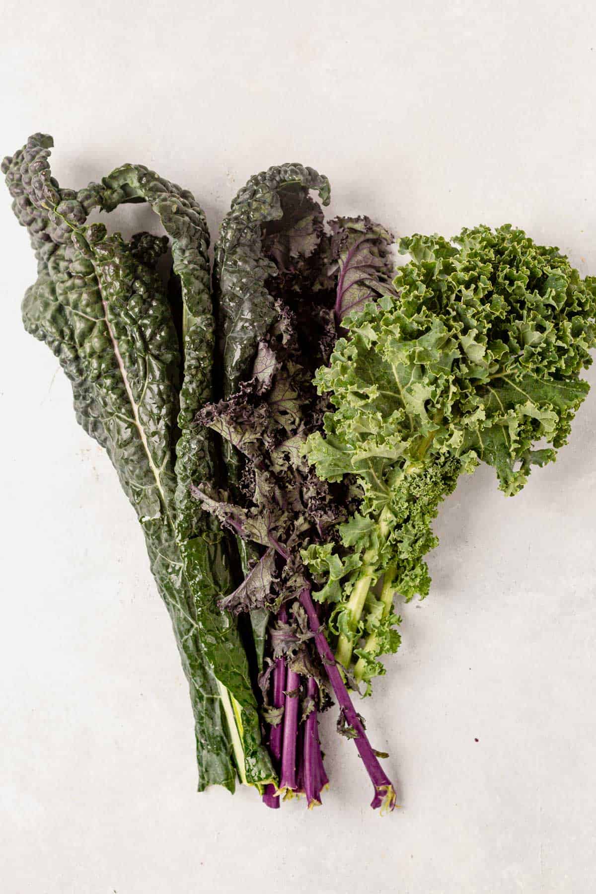 three types of raw kale on a countertop