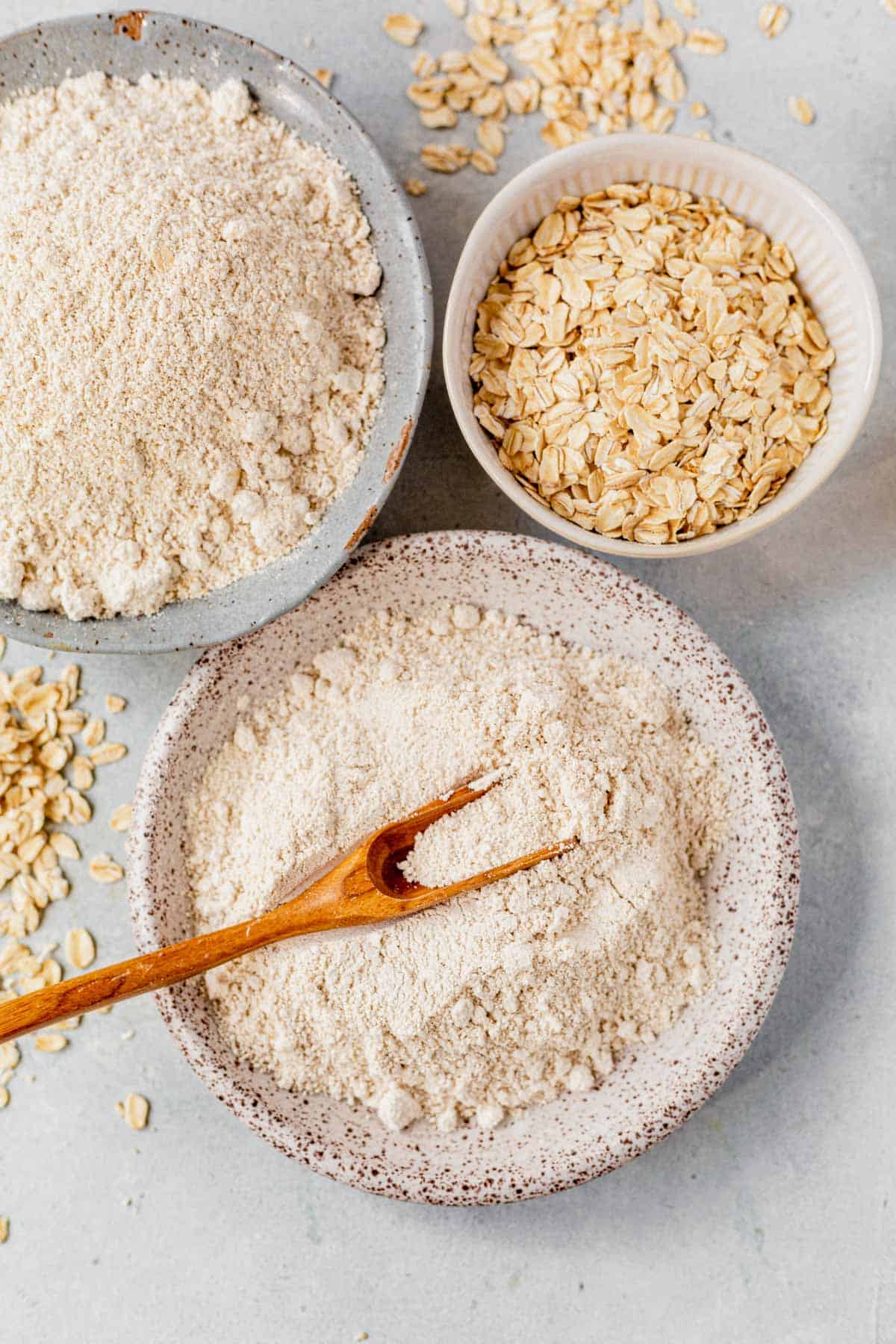oat flour in a bowl with a spoon next to a bowl of rolled oats