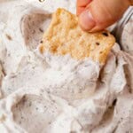 hand dipping into a bowl of homemade boursin cheese with a cracker.