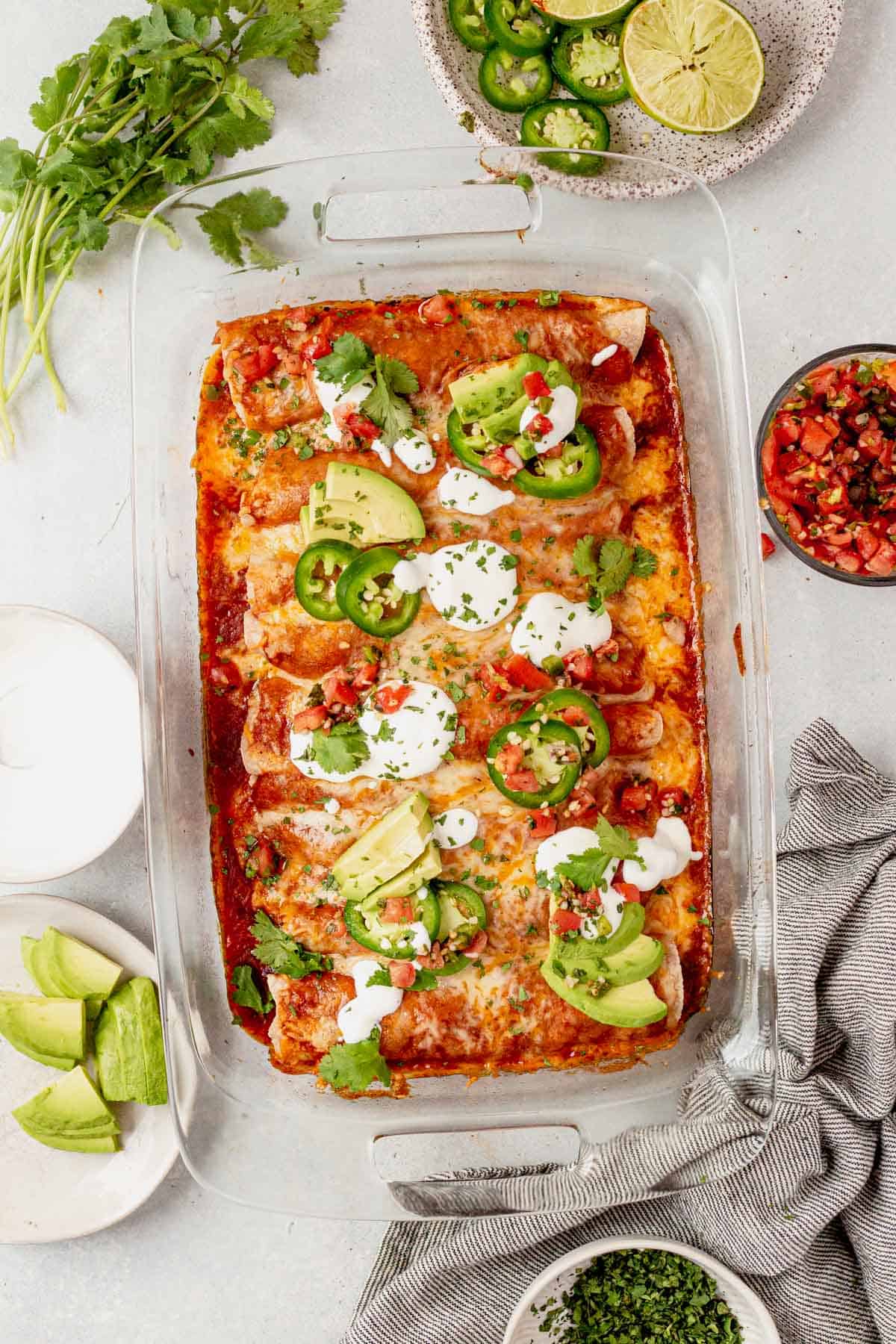 a pan of shredded beef enchiladas with sour cream, avocado, and cilantro