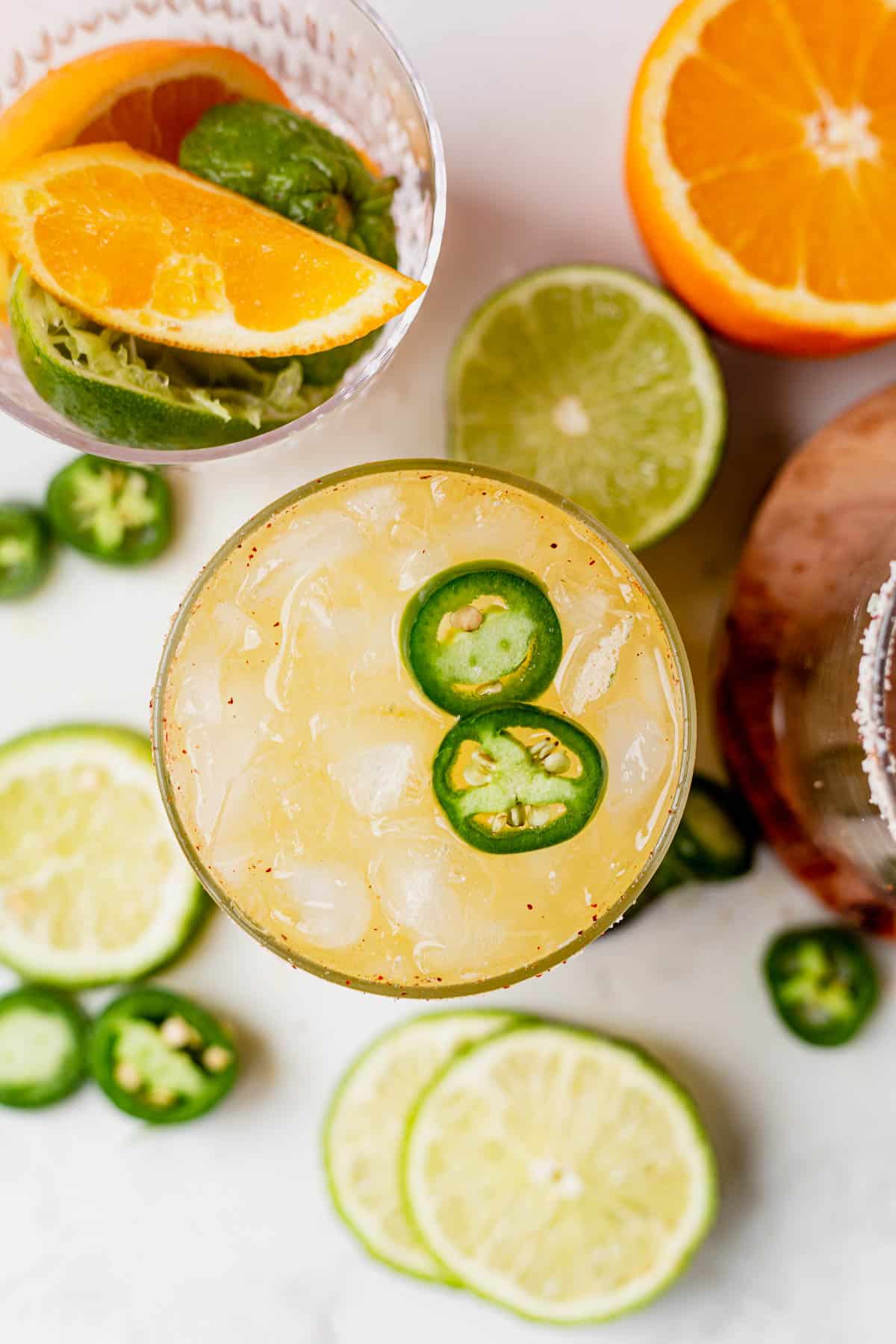 a glass full of a skinny spicy margarita with fresh limes and oranges
