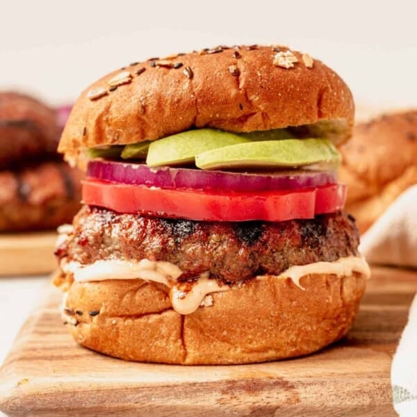 grilled hamburger on a bun with onion, tomato, and avocado