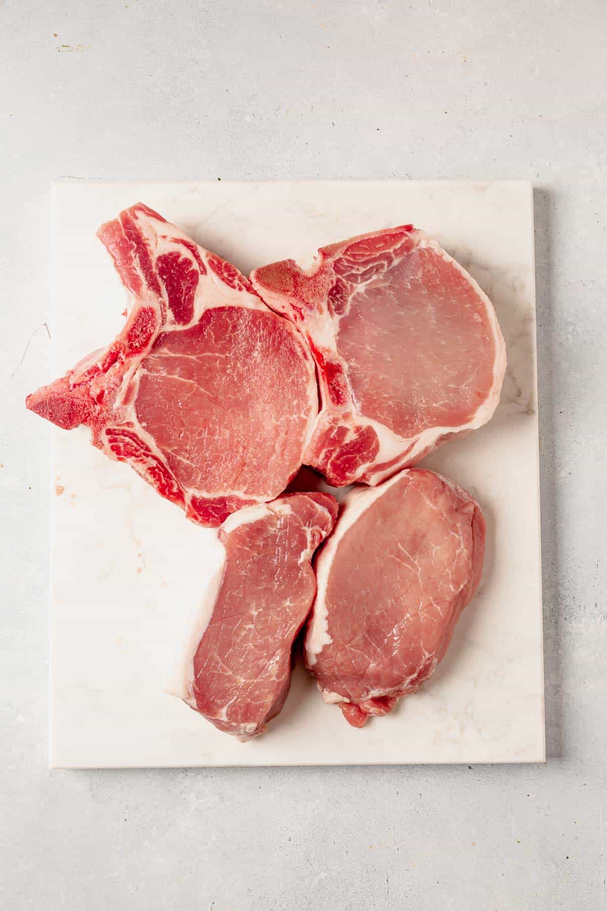 2 raw boneless and 2 bone in pork chops on a cutting board