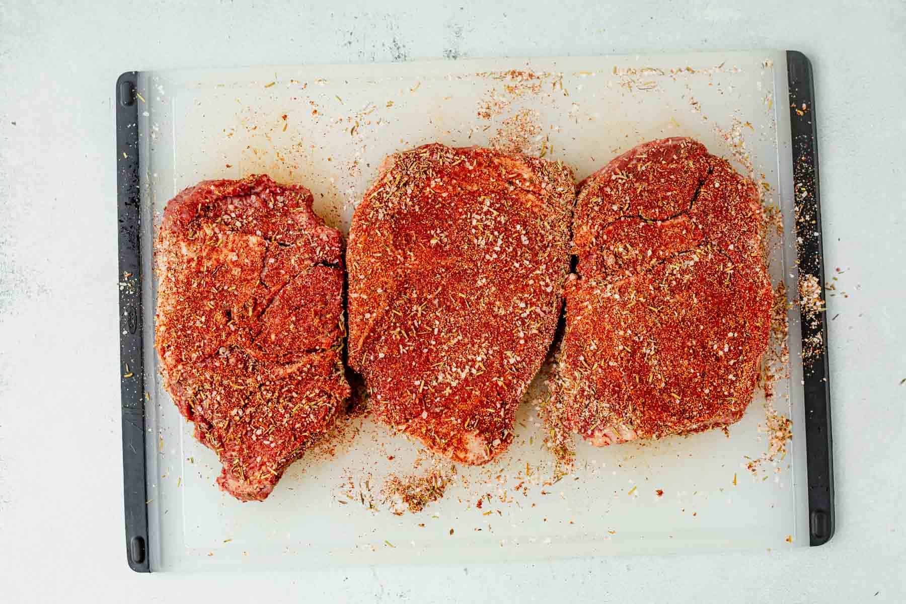three ribeye steaks coated in steak seasoning