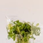 a bunch of fresh cilantro inside a glass jar with water with an open ziploc bag at the base