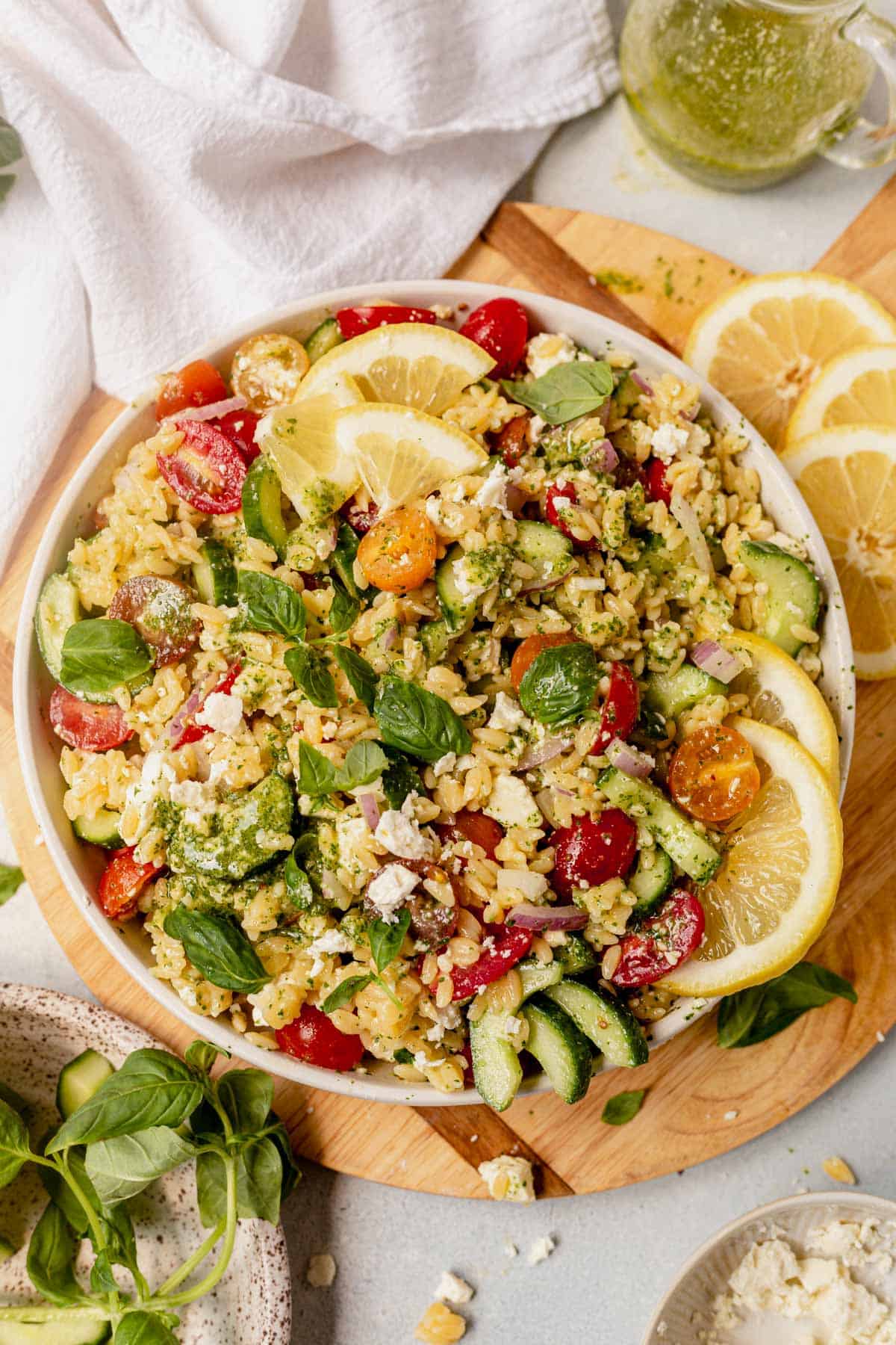 lemon orzo pasta salad  in a large bowl on a round wooden cutting board