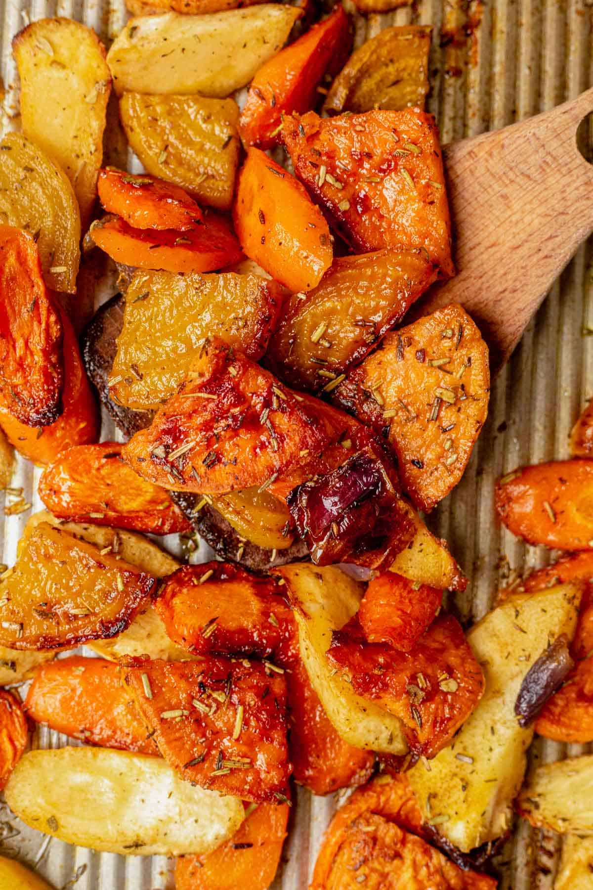 scooping roasted root vegetables off a baking sheet