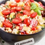 black serving bowl filled with an easy recipe for fresh summer corn salad on a table with an ear of corn