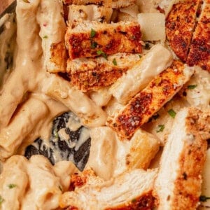 Close-up of creamy garlic parmesan chicken pasta, topped with sliced, seasoned seared chicken breast and a sprinkle of fresh chopped herbs.