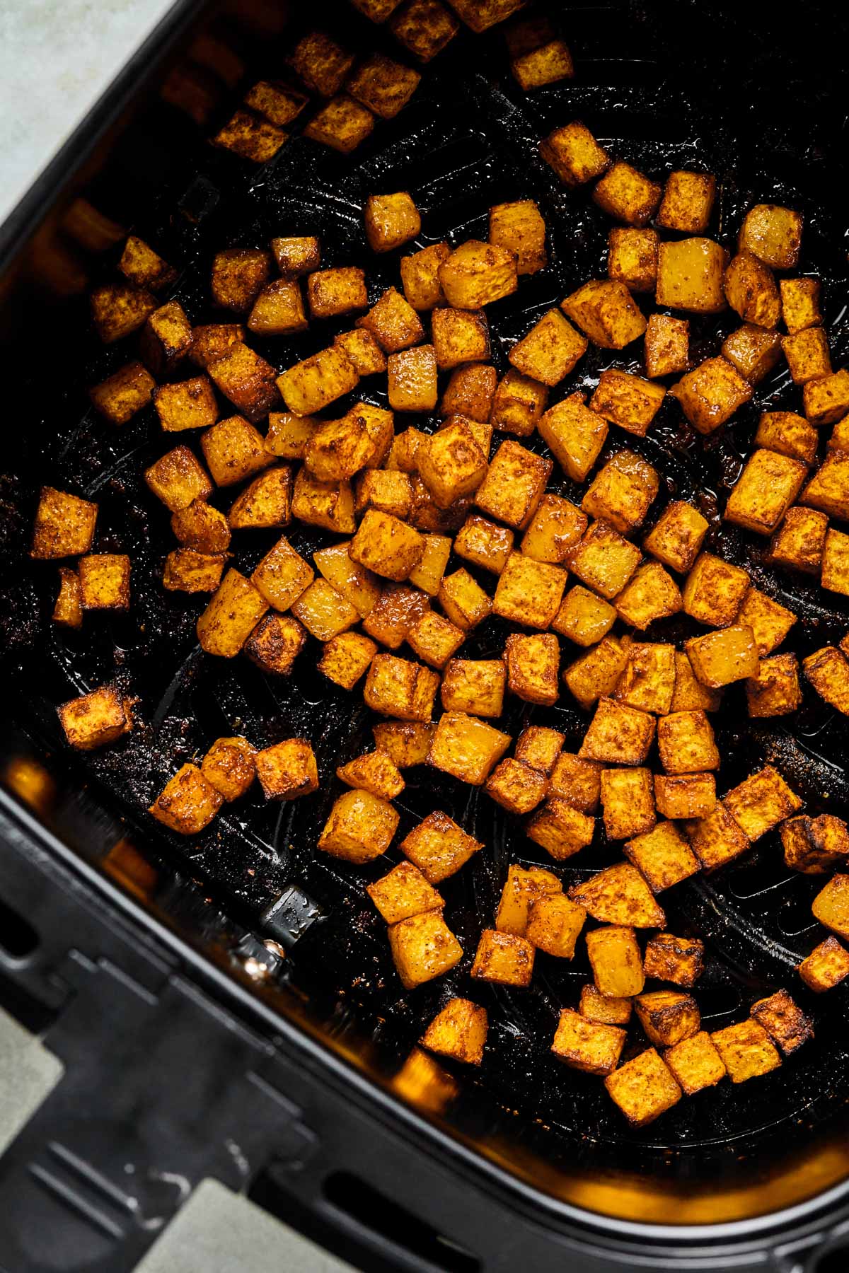 Golden brown air fryer butternut squash cubes with crisp caramelized edges inside a dark air fryer basket.