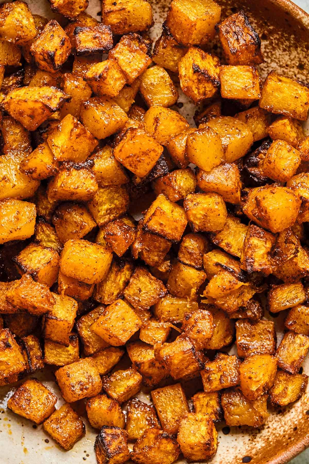 Close-up of crispy, caramelized butternut squash served on a rustic brown and white plate.