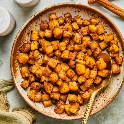 Caramelized air fryer butternut squash served in a rustic speckled bowl with a gold spoon, ready to serve.