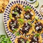 mexican chorizo tacos on a plate with onion, cilantro, and lime wedges.