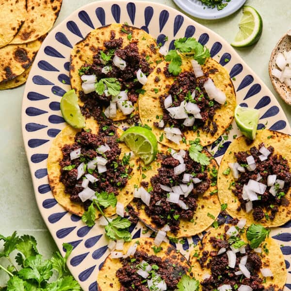 mexican chorizo tacos on a plate with onion, cilantro, and lime wedges.