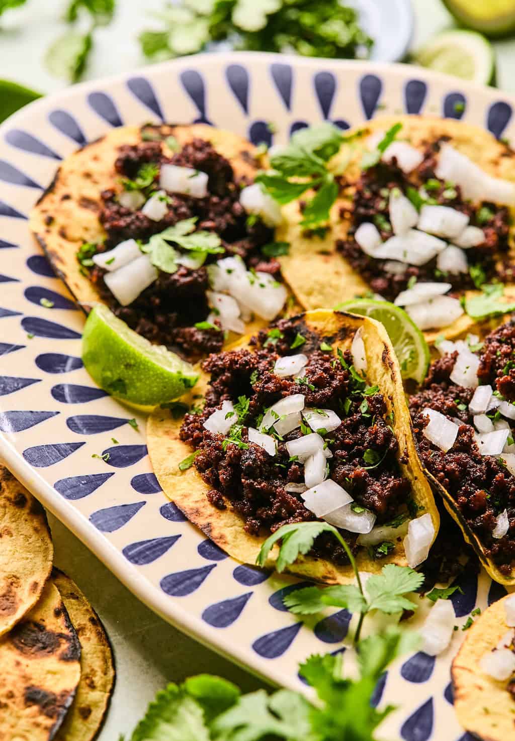 chorizo tacos on a plate with onion, lime wedges, and cilantro.