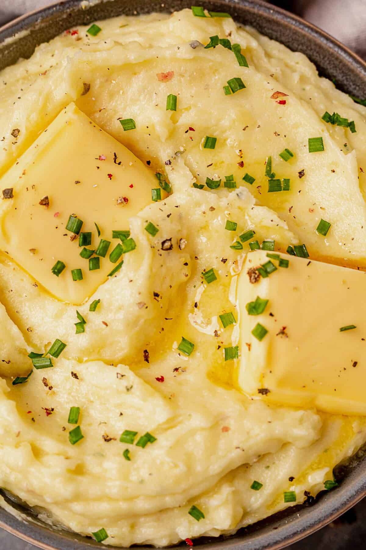 half melted butter on top of a bowl of boursin mashed potatoes with fresh chives.