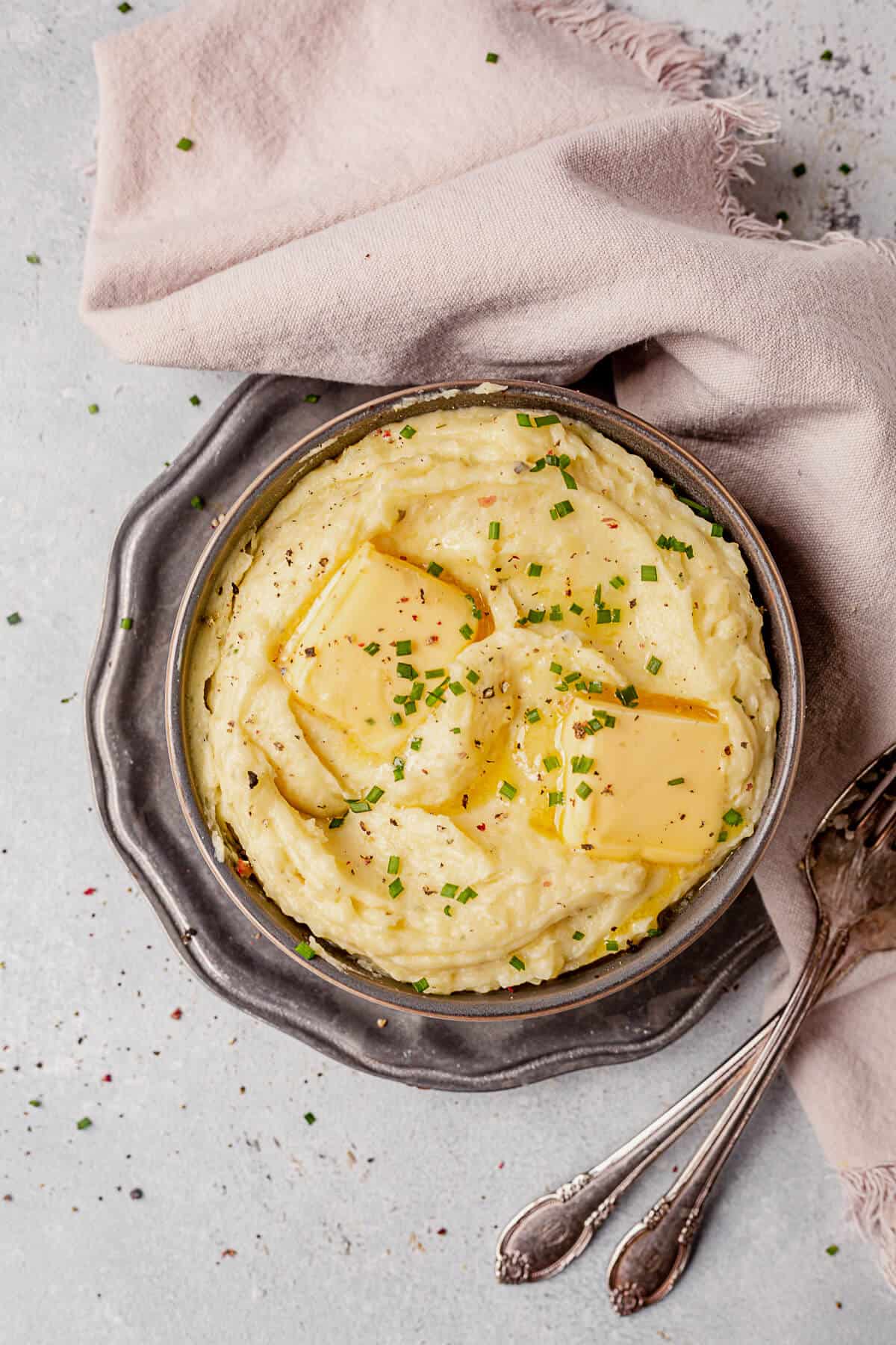 a bowl of boursin mashed potatoes with butter and chopped chives on top.