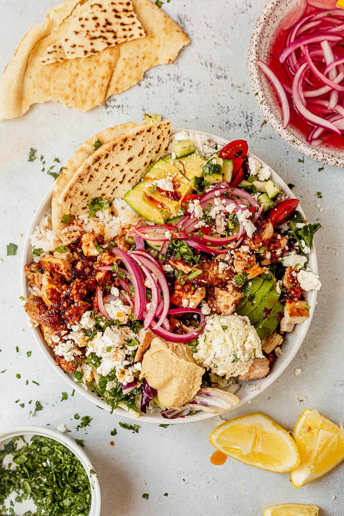 cava inspired honey harissa chicken bowl on a countertop with a side of pita bread