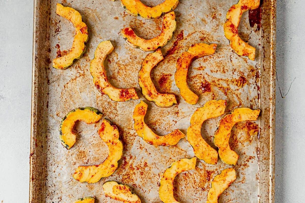 delicata squash cut into half moons on a sheet pan with olive oil, garlic, and paprika