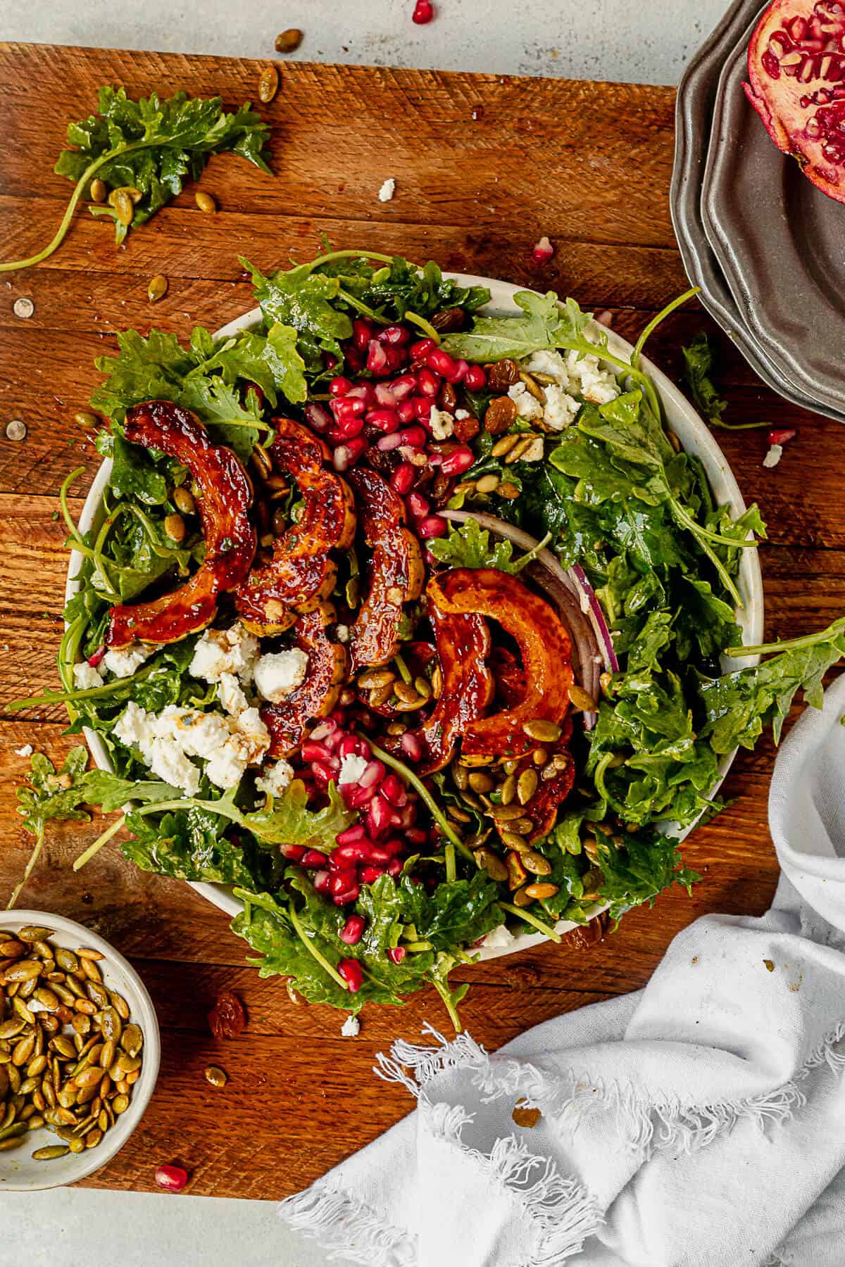 a large salad in a bowl with greens, roasted delicata squash, pumpkin seeds, pomegranate, and vinaigrette