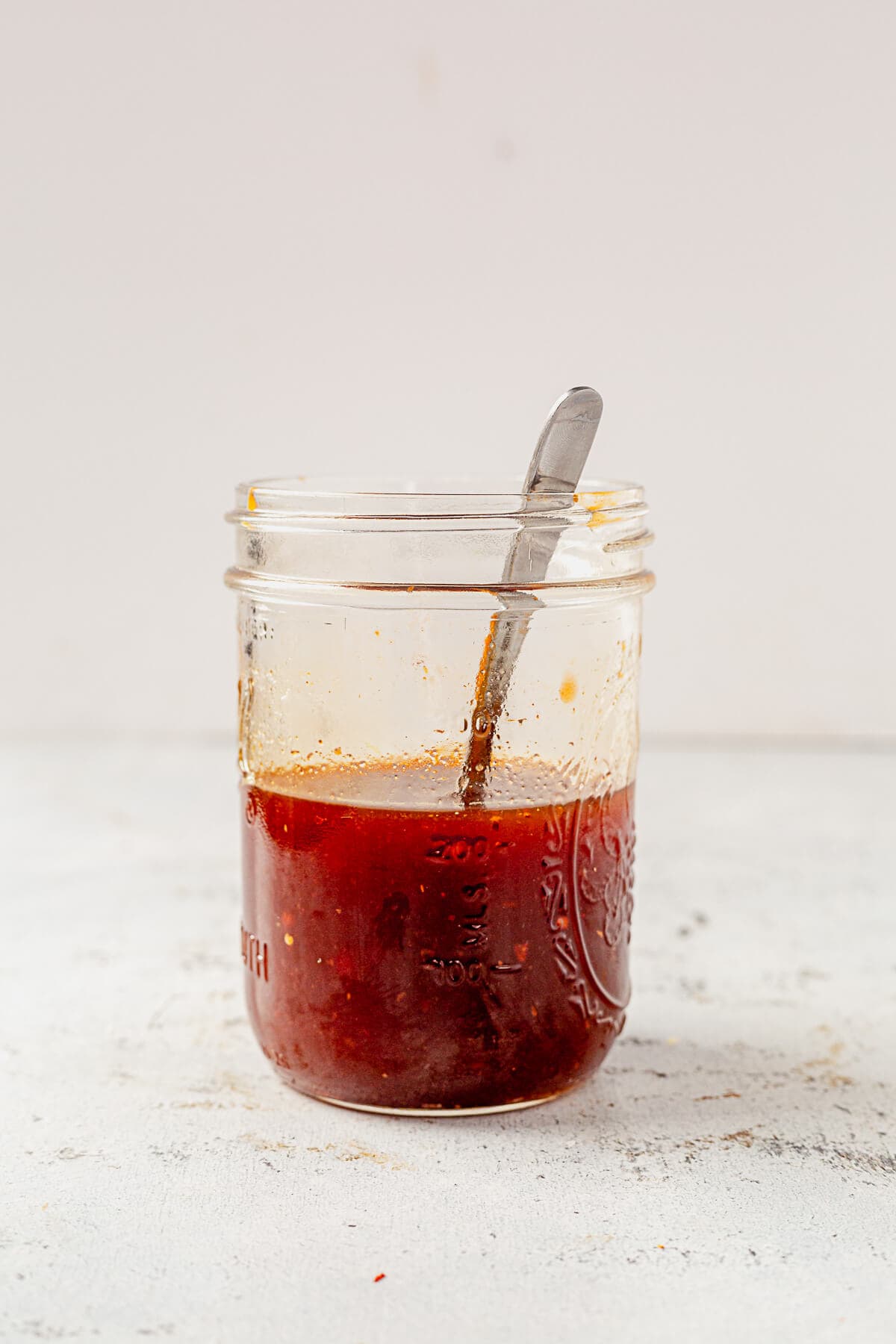 a mason jar full of spicy firecracker sauce with a serving spoon