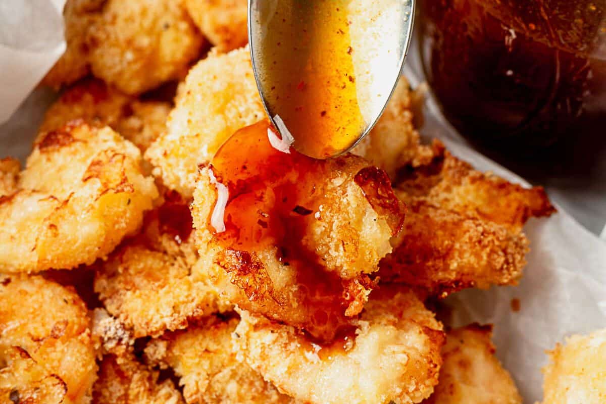 spooning firecracker sauce on top of breaded shrimp in a dish