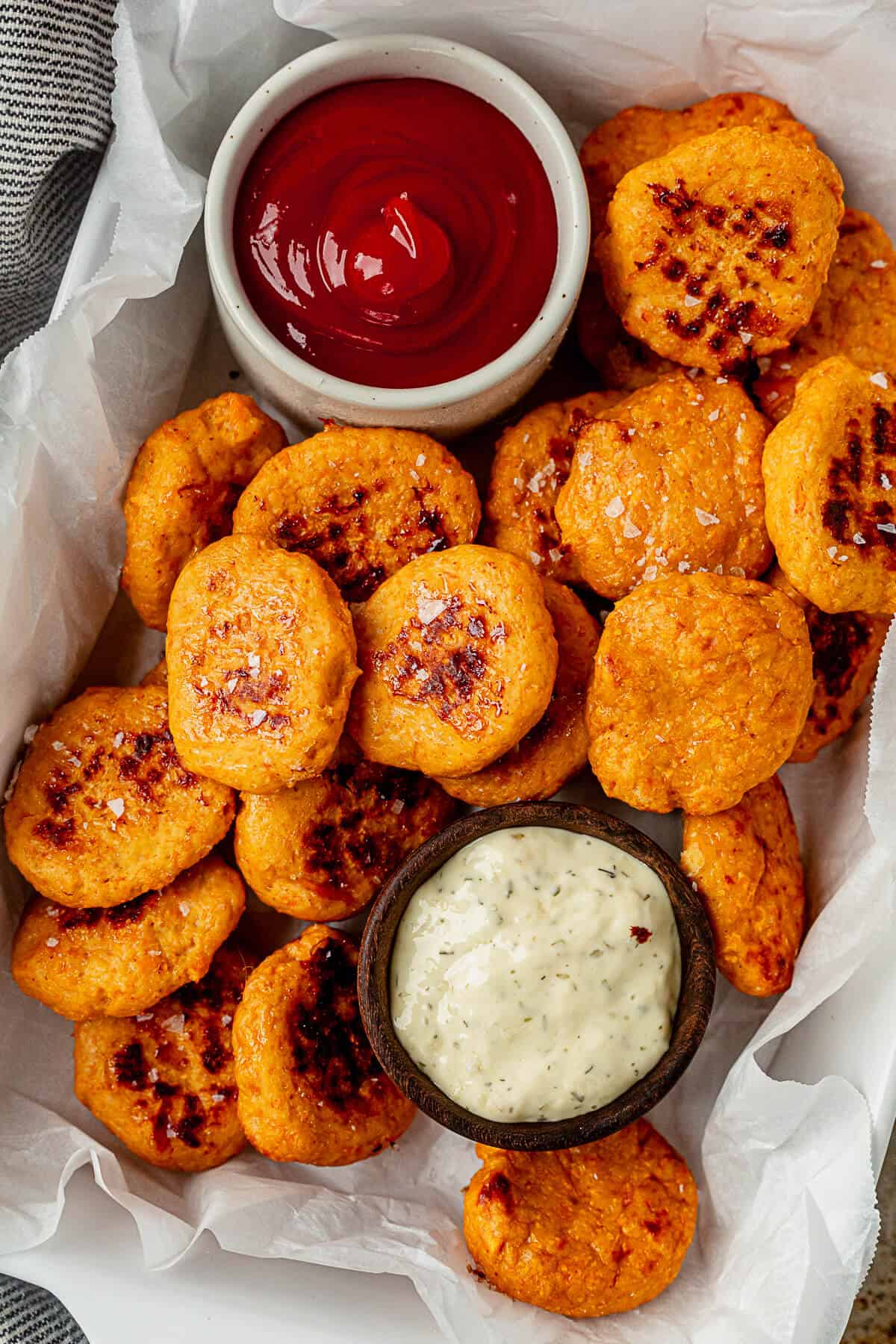 healthy chicken nuggets cooked golden brown in a parchment lined tray with ketchup and ranch