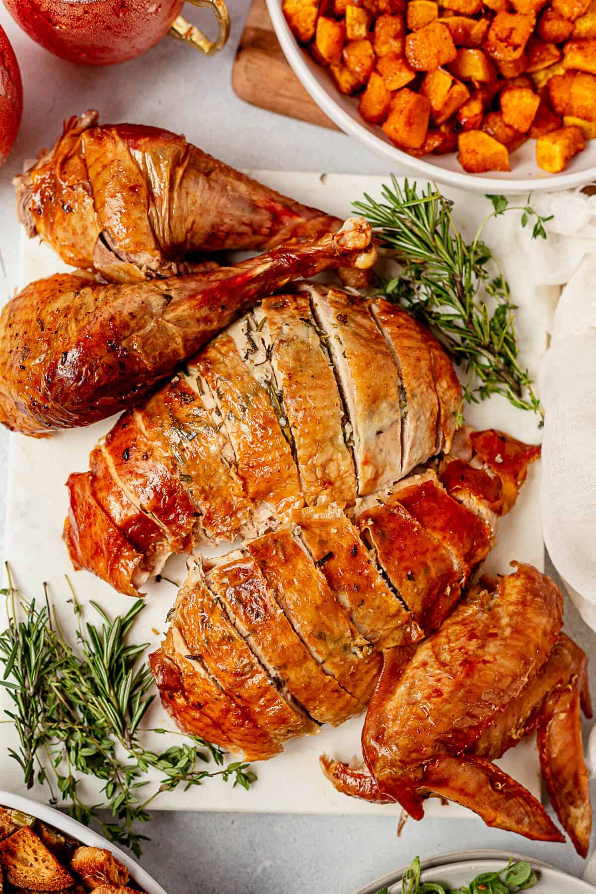 carved turkey breast and turkey legs on a platter with herbs and side dishes