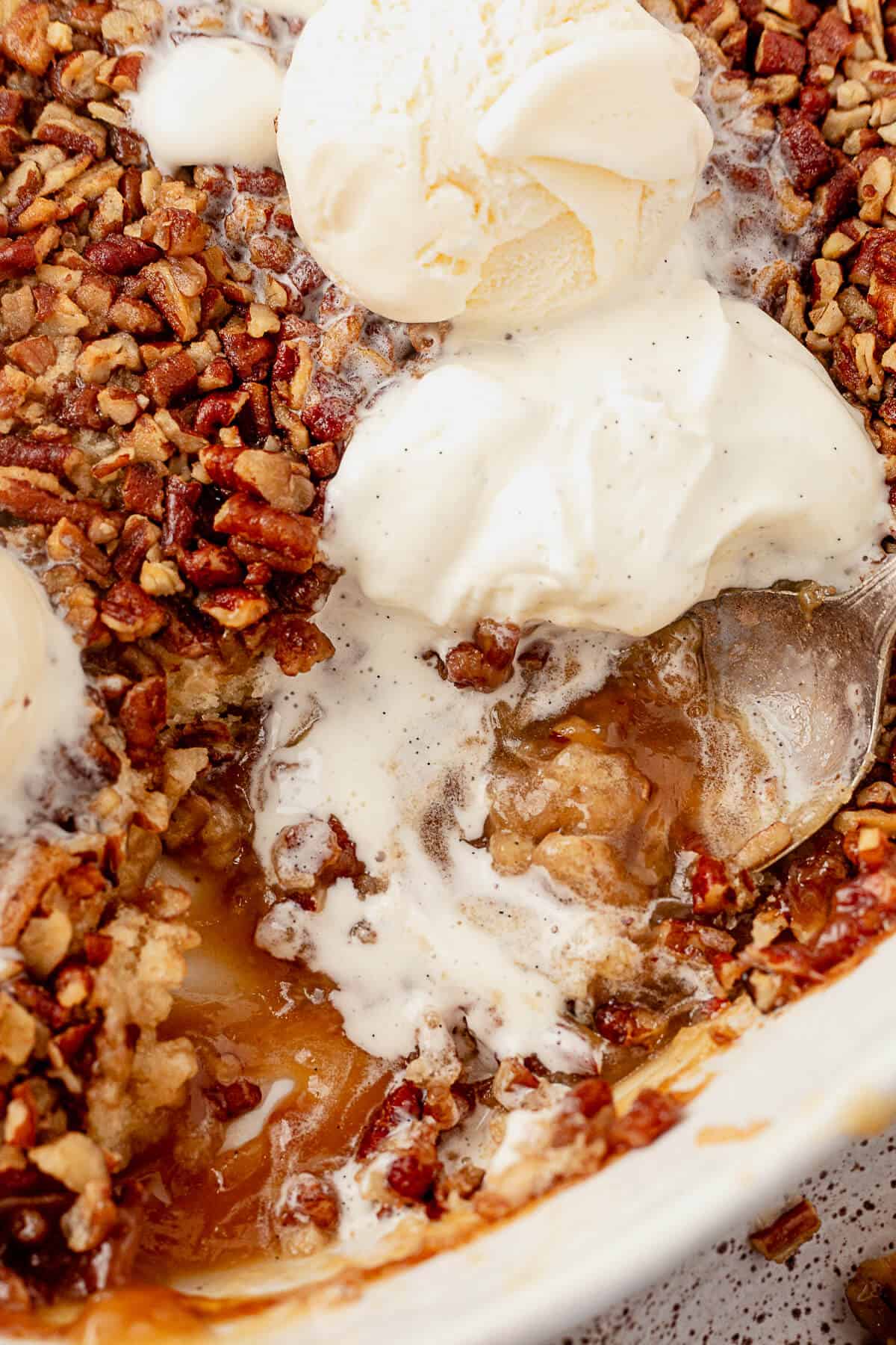 half melted whipped cream and ice cream on top of pecan pie cobbler in the casserole dish