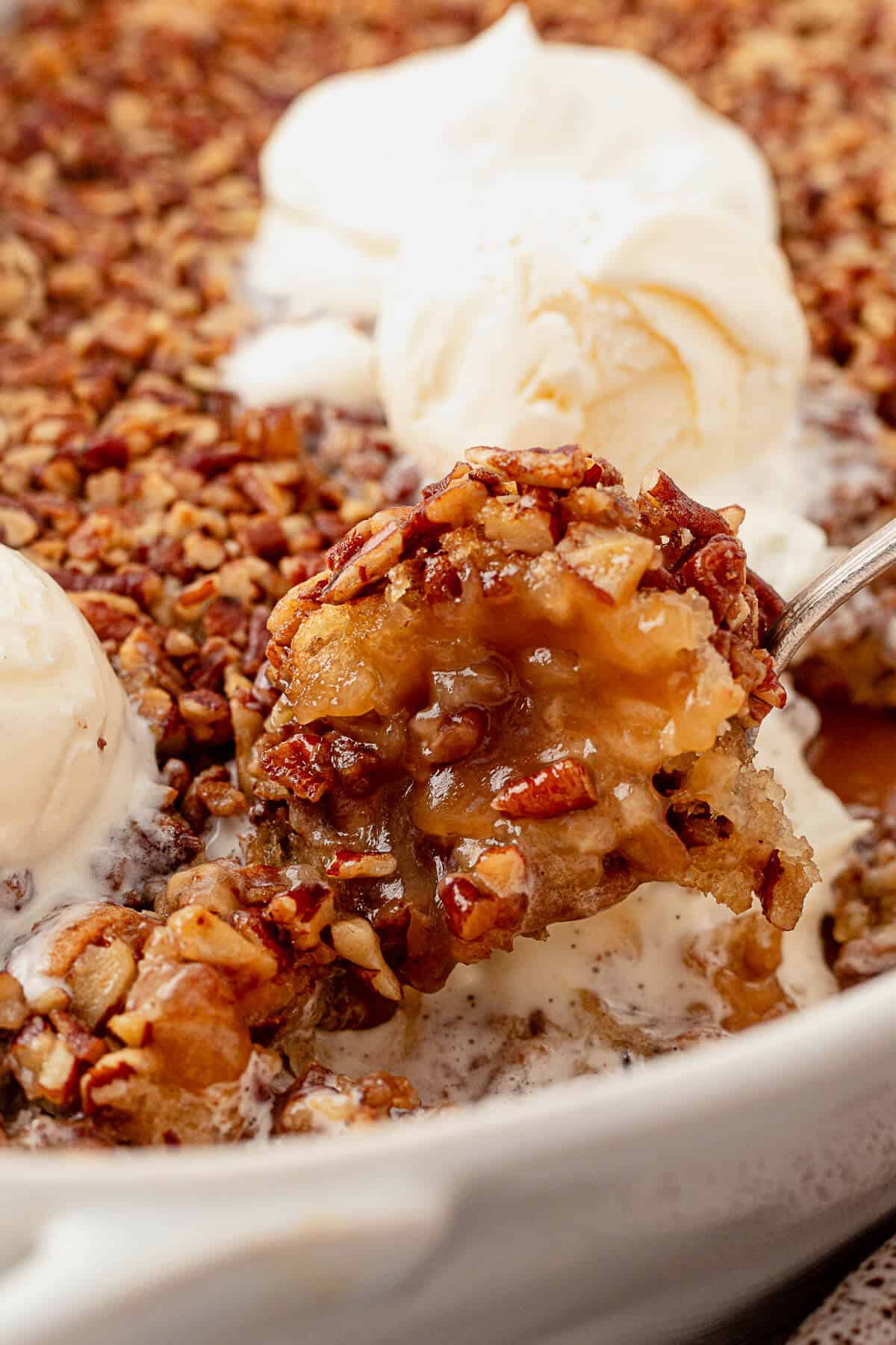 a large serving spoon scooping pecan pie cobbler out of a casserole dish