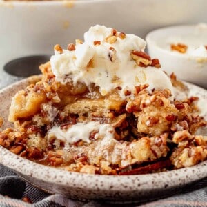 a large serving of gooey pecan pie cobbler in a dish with whipped cream and a bite taken out