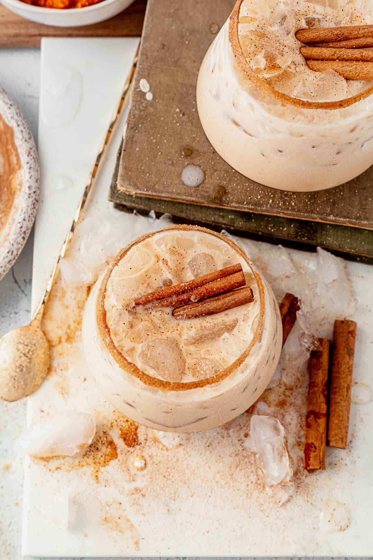 two pumpkin spice white russians on a countertop garnished with cinnamon sticks and more cinnamono