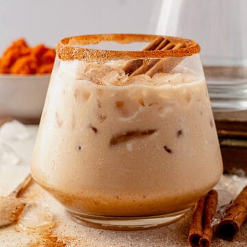 creamy pumpkin spice white russian in a ball glass with a cinnamon sugar rim and garnished with cinnamon sticks