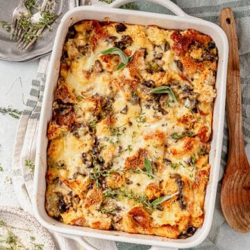 savory bread pudding with mushrooms and gruyere in a casserole dish with fresh herbs