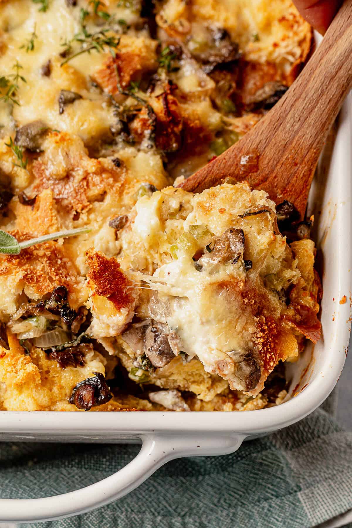 scooping savory bread pudding out of a 3 quart casserole dish showing the melted cheese