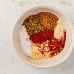 Bowl filled with a colorful blend of paprika, oregano, saffron, salt, and other spices for Spanish chicken and rice.
