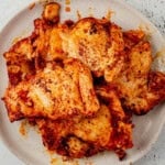 Boneless chicken thighs coated in a Spanish spice rub on a white plate, after searing.