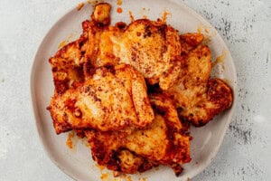 Boneless chicken thighs coated in a Spanish spice rub on a white plate, after searing.