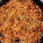 Uncooked white rice being toasted in a cast iron skillet with shallots and spices.
