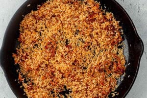 Uncooked white rice being toasted in a cast iron skillet with shallots and spices.