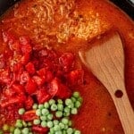 Cast iron skillet filled with broth, fire-roasted tomatoes, and frozen peas before simmering.