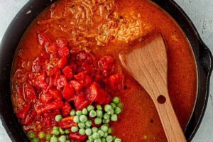 Cast iron skillet filled with broth, fire-roasted tomatoes, and frozen peas before simmering.