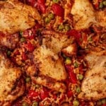 Cooked Spanish chicken and rice in a skillet with golden chicken thighs, tomatoes, and peas.