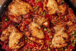 Cooked Spanish chicken and rice in a skillet with golden chicken thighs, tomatoes, and peas.