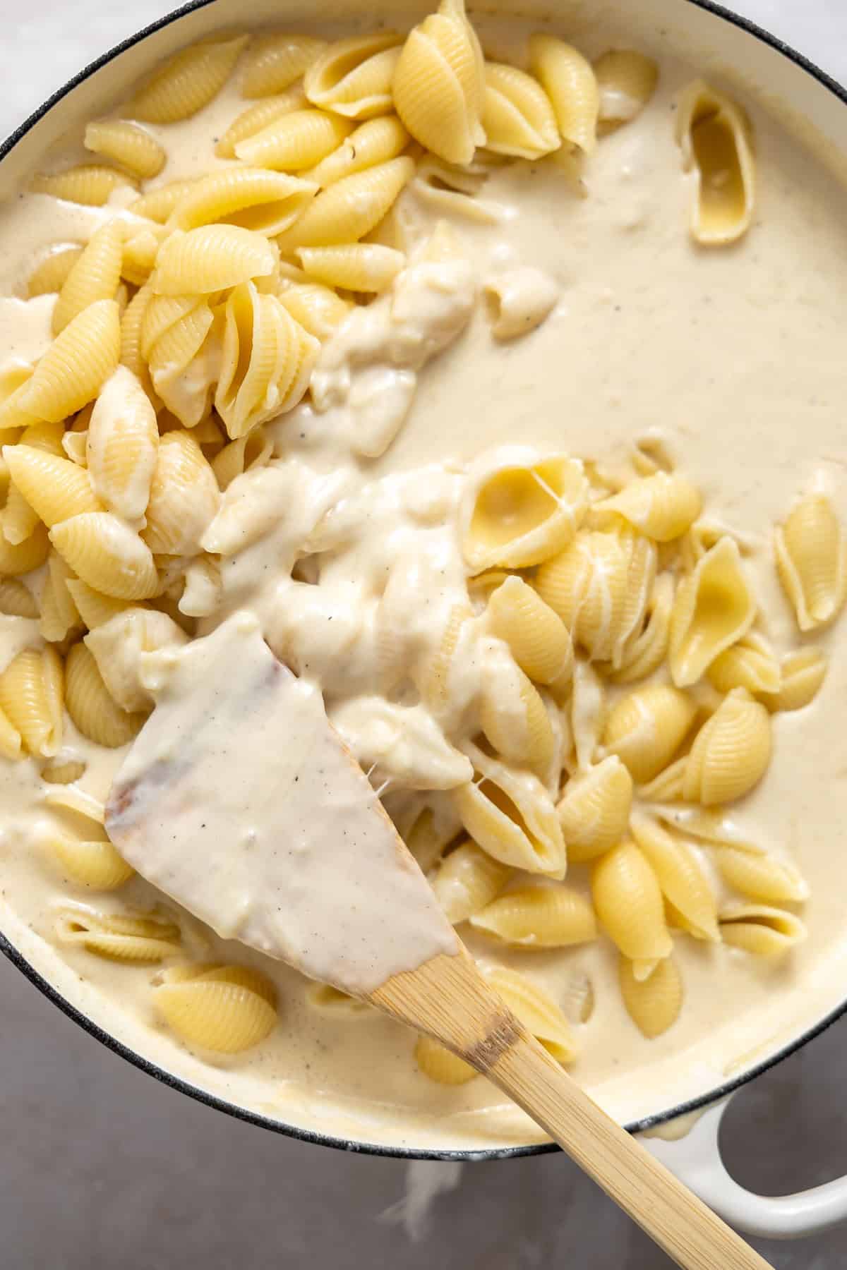 stirring cooked pasta shells into a white cheddar sauce on the stove top.