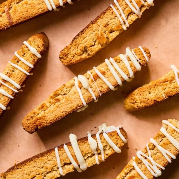 Eight gluten free almond flour biscotti cookies arranged on parchment paper, drizzled with white icing. The cookies are golden brown and have a crunchy texture.